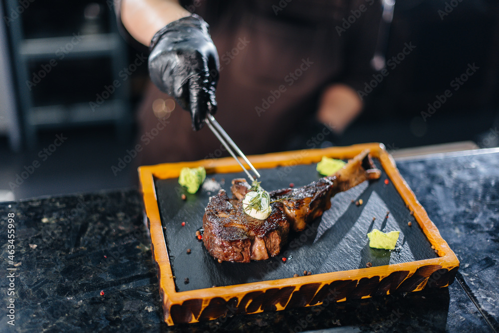 Fototapeta premium A professional chef beautifully serves a juicy grilled steak with butter and seasonings. Grilled meat in a restaurant.