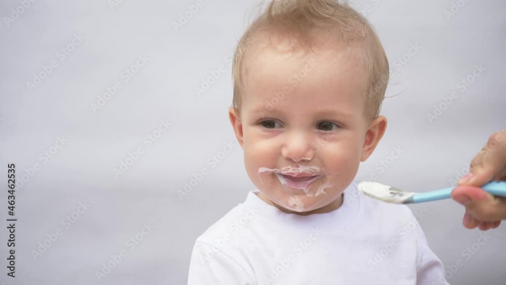 mother feeds her little son from a spoon with porridge. The kid is eating breakfast from a spoon. loving mother takes care of the child, spoon feeds porridge. Handsome smiling cute kid. Children food mother feeds her little son from a spoon with porridge. The kid is eating breakfast from a spoon. loving mother takes care of the child, spoon feeds porridge. Handsome smiling cute kid. Children food