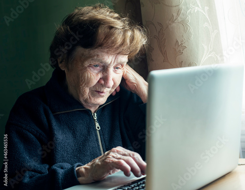 An old woman studying on the computer in her home.