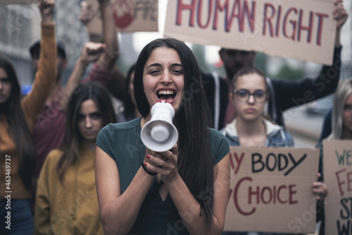 Group of young people protesting on the street with signs raised to promote women rights and right to abortion. Focus on the woman in front screaming to the megaphone