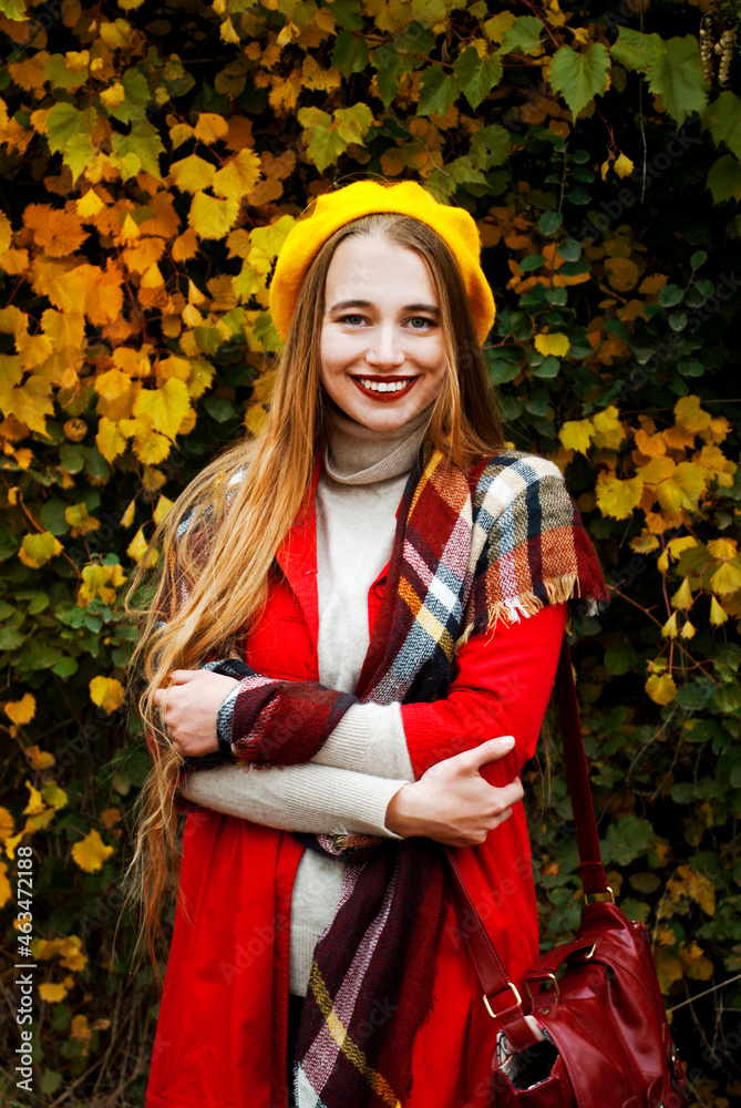 Portrait of a beautiful blonde woman in an autumn park. Female autumn style. Warm artwork. Smiles and looks at the camera