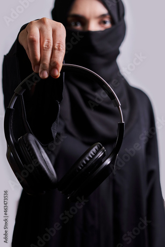 Muslim woman in traditional hijab clothing holding black wireless headphones photo