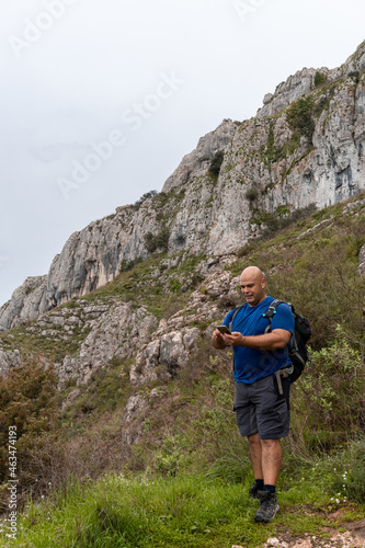 Selective focus on a muscular Caucasian man and hiker in the mountains, using the smartphone.