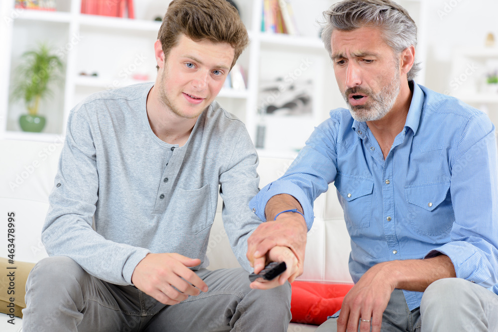 Boy changing channel on television, man objecting Boy changing channel on television, man objecting