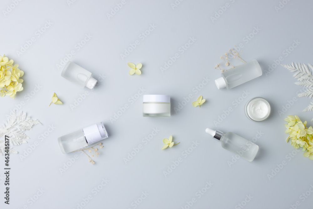 Naklejka premium Cosmetic skin care products with with flowers on grey background. Flat lay, copy space