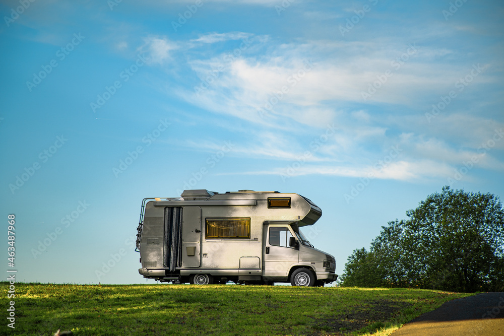 Closeup shot of a camper van parked in the green field under the blue sky - obrazy, fototapety, plakaty 