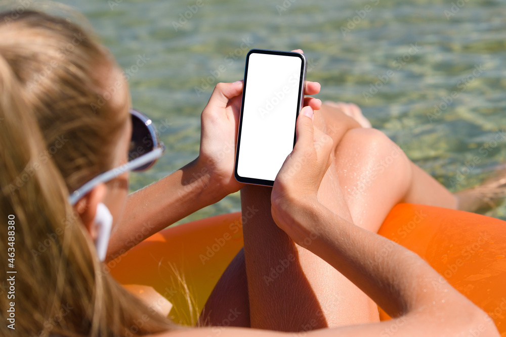 Girl in the sea sunbathes with a smartphone in her hands
