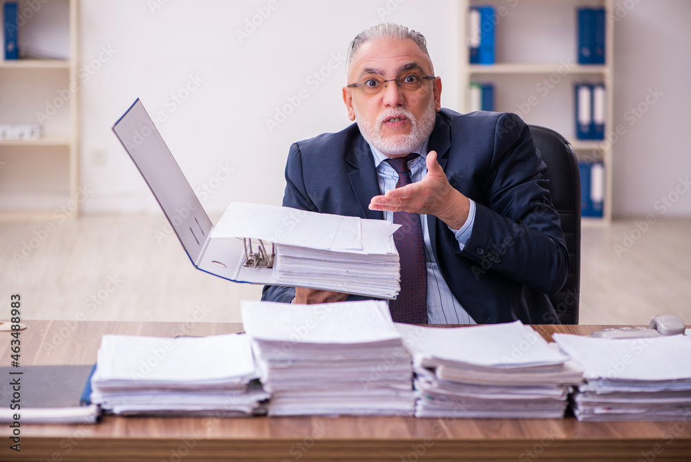 Old businessman employee unhappy with excessive work in the office Old businessman employee unhappy with excessive work in the office