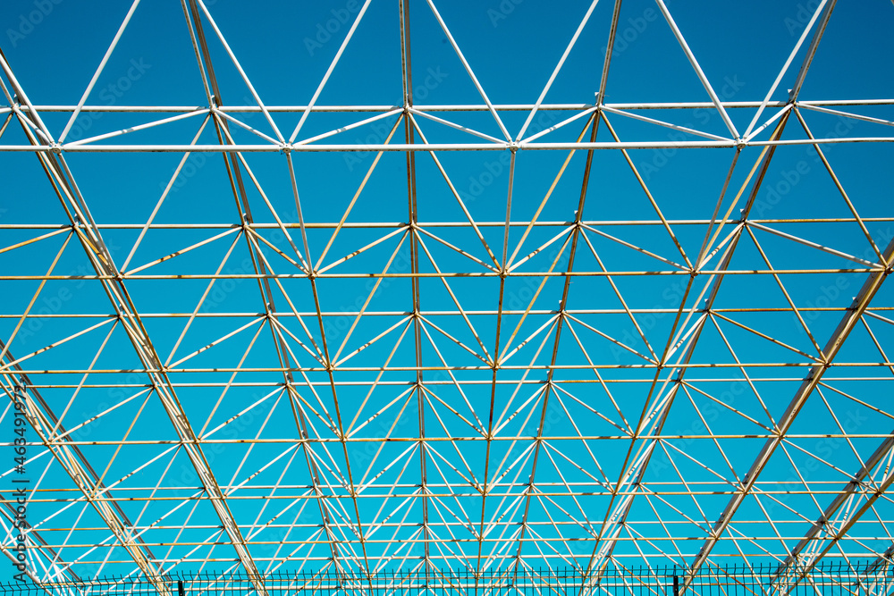 Obraz premium Openwork metal construction on a blue sky background on a clear sunny day, texture backgrounds for graphic design. Abstract wallpaper.