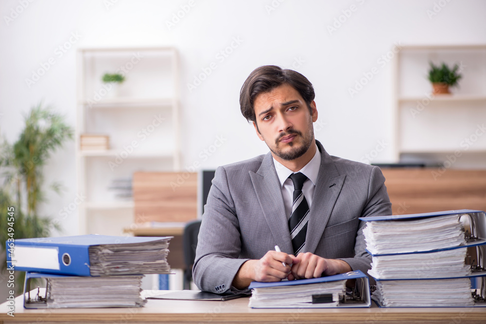 Young male employee unhappy with excessive work in the office Young male employee unhappy with excessive work in the office