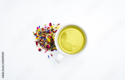 Dried herbal tea leaves next to a cup of hot, freshly brewed tea on a white background. Table top view, flat lay, copy space.