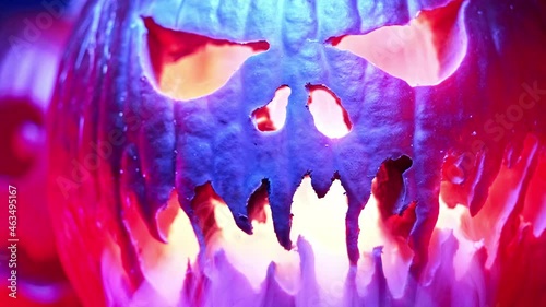 Scary carved halloween pumpkins with smoke under colorful neon light. Trick or treat background. Glowing face with flame inside. Symbol of All Hallows' Eve. Slow motion