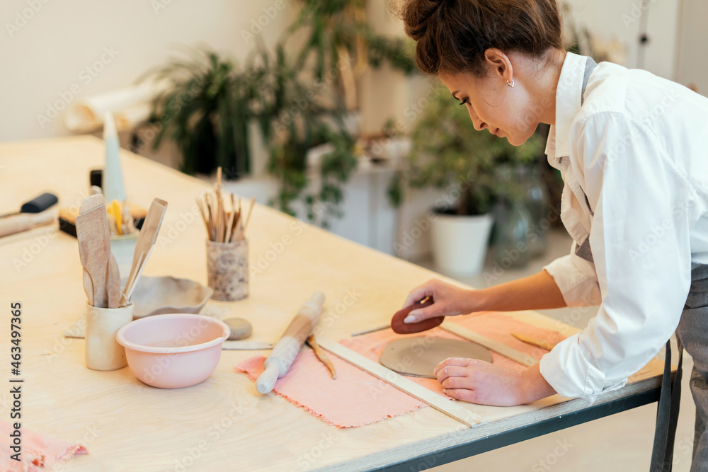 A uniformed employee in the workshop. Handmade to order. A woman works in a studio making dishes out of clay. Master of ceramics and glass for design.