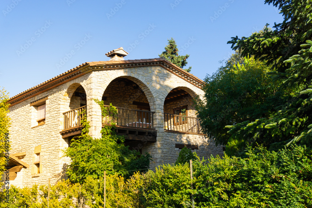 Stone chalet with arches on the porch and wooden roof in the town of Tavertet