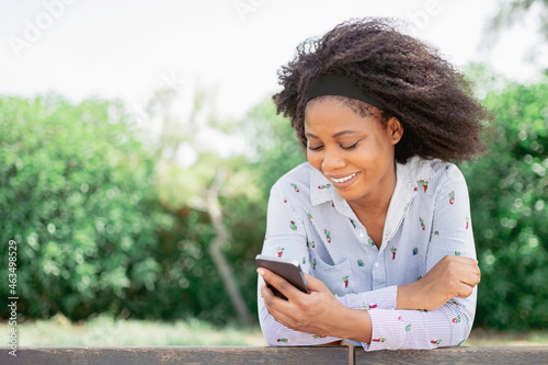 View of a cheerful African American woman smiling while using her mobile phone outdoors.
