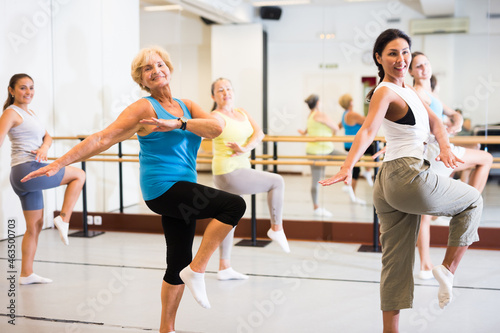 Portrait of smiling mature woman practicing ballet dance moves during group class in choreographic studio © JackF