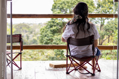 woman from the back watching the woods from the porch of a log cabin