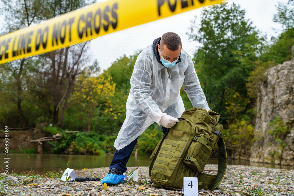 Forensic police investigator collecting evidence at the crime scene by the river in nature Forensic police investigator collecting evidence at the crime scene by the river in nature