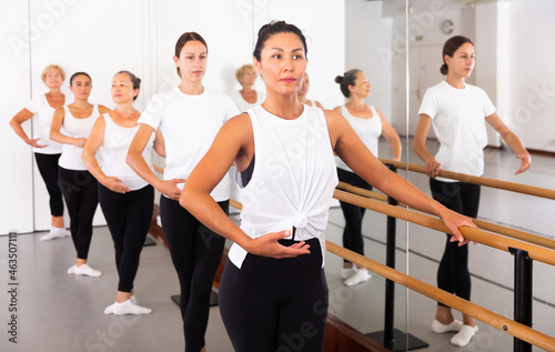 Women of different ages exercising ballet moves in training room. © JackF