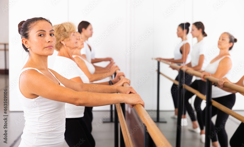 Portrait of a focused latin american woman in a group class, doing demi plie near the ballet barre, standing in the 2nd ..position of the ballet stance. Close-up portrait