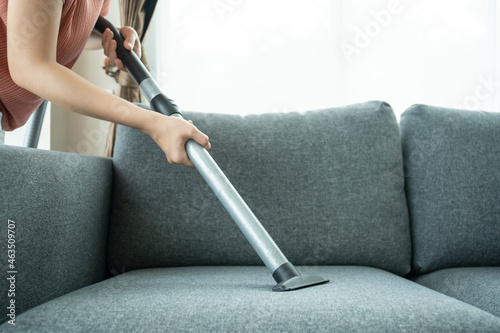 Asian housewife using a wireless vacuum machine to clean a sofa in living room.