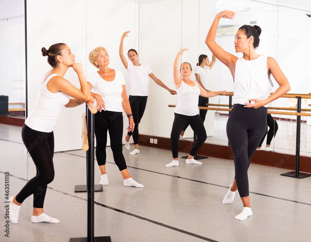 Fototapeta premium Asian woman demonstraiting ballet moves in front of women of different ages during group ballet training.