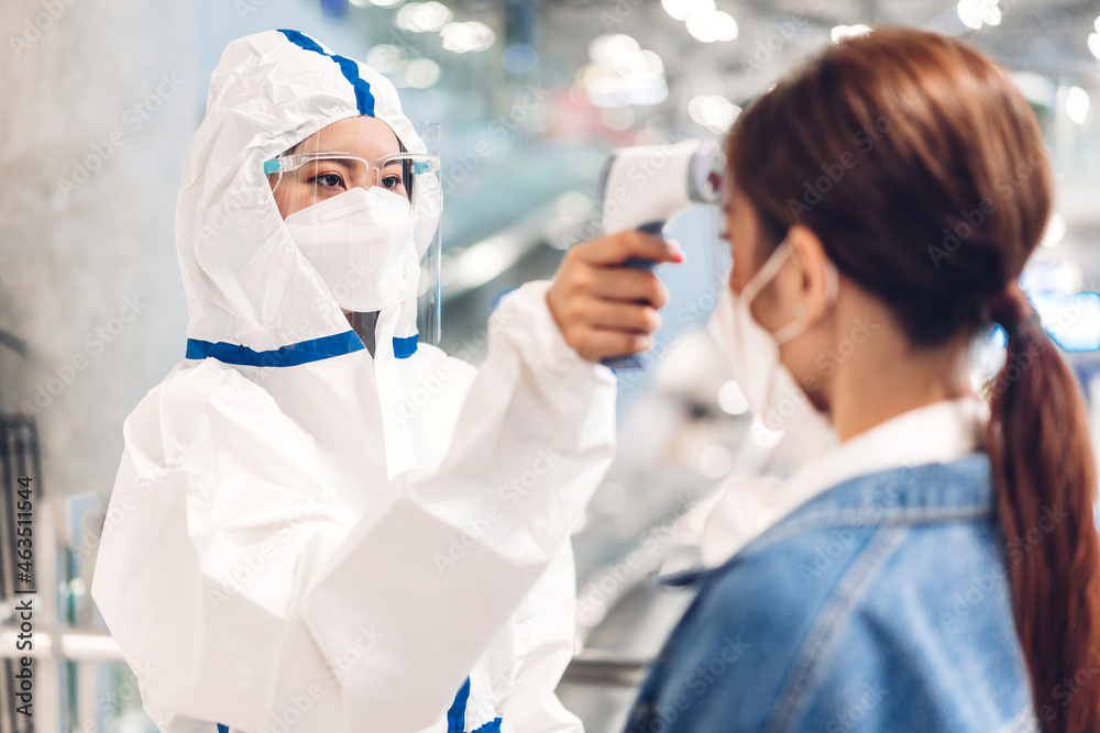 Doctor woman with protective suit use infrared forehead thermometer for checking body temperature scan woman patient fever in quarantine for coronavirus wearing safety protective mask at hospital
