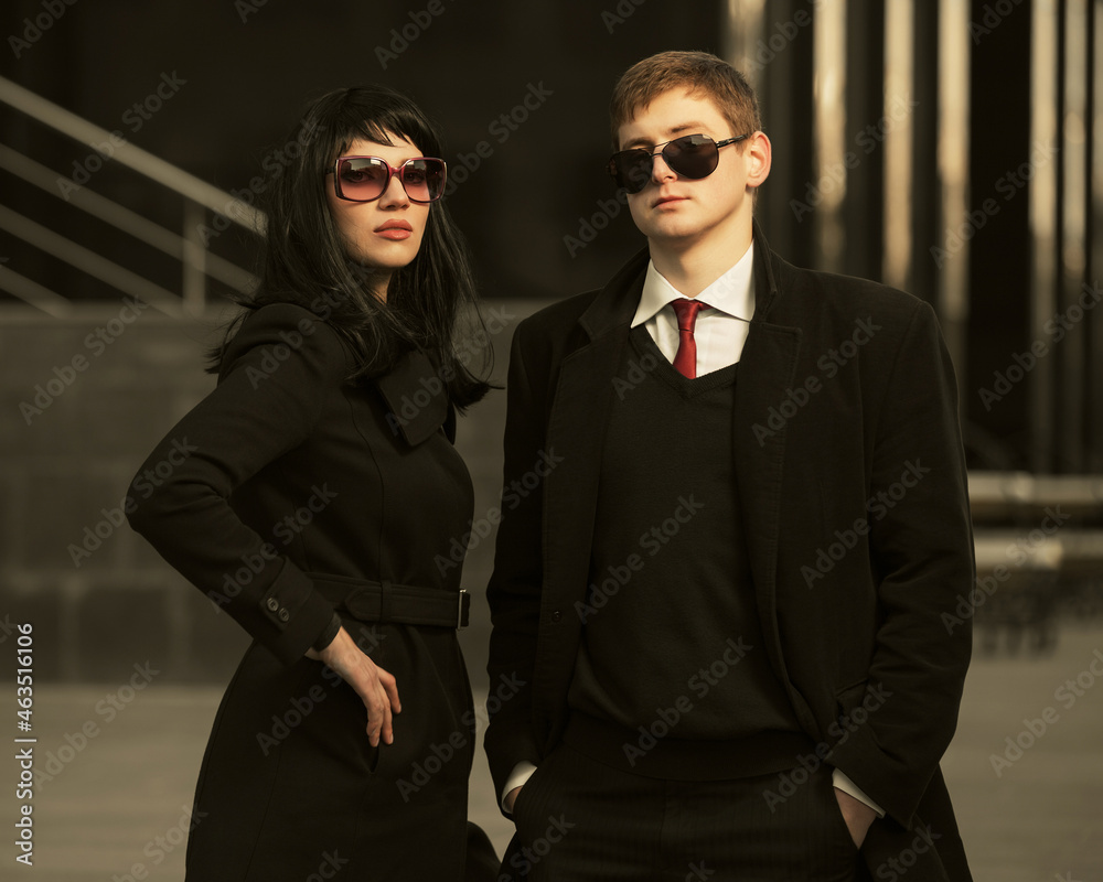 Young fashion business couple in classic black coats and sunglasses