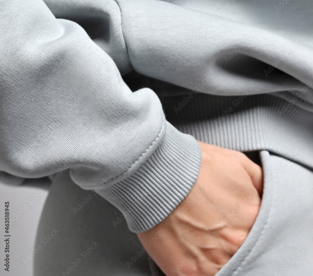 Closeup of slim sporty woman in grey sports suit, sportswear hoodie and pants standing sideways, holding hand in her pocket