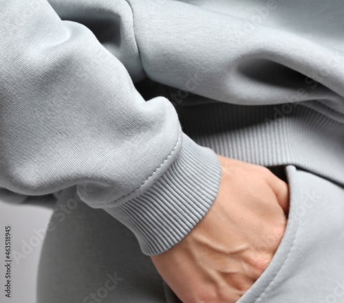 Closeup of slim sporty woman in grey sports suit, sportswear hoodie and pants standing sideways, holding hand in her pocket