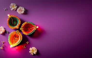 Happy Diwali - Clay Diya lamps lit during Dipavali, Hindu festival of lights celebration. Colorful traditional oil lamp diya on purple background
