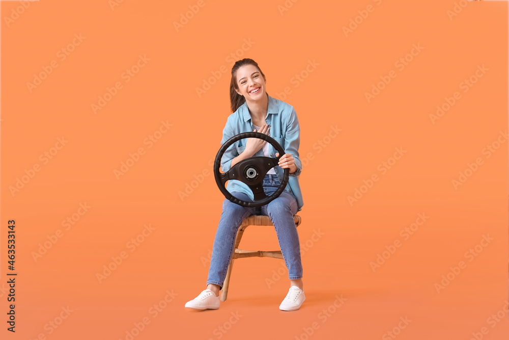 Young woman with steering wheel sitting in chair on color background Young woman with steering wheel sitting in chair on color background