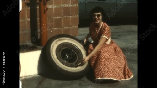 Woman Changing Tire 1949 - A woman in a pretty dress adds air to a tire.   photo