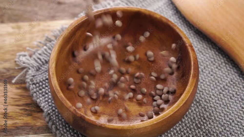 Uncooked ingredient brown lentils falling into a wooden bowl on a rough jute napkin in slow motion. Close up. On a rustic wood table Uncooked ingredient brown lentils falling into a wooden bowl on a rough jute napkin in slow motion. Close up. On a rustic wood table