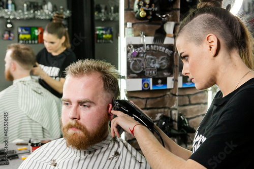 a red-haired adult man is cut by a girl in a barbershop