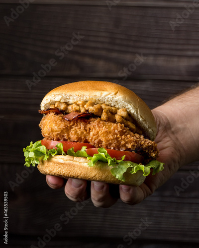 Holding lettuce, tomato, bacon and crispy chicken burger 