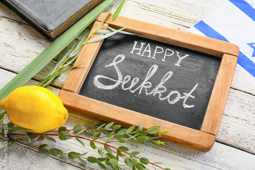 Chalkboard with text HAPPY SUKKOT and festival symbols on light wooden background photo