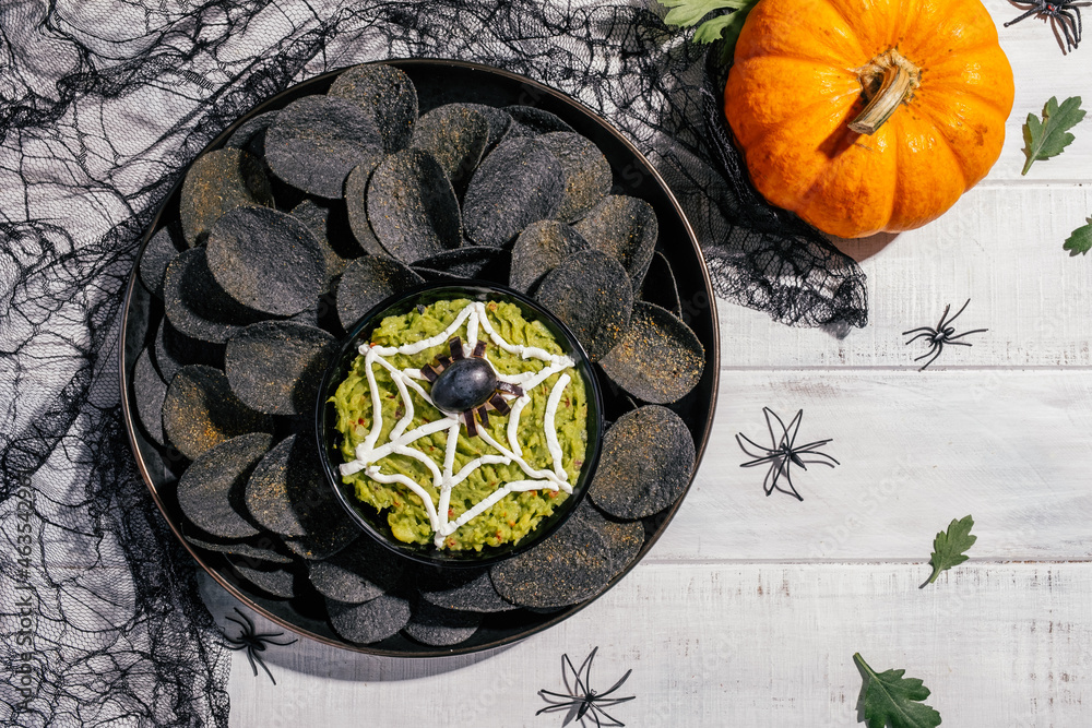 Spooky Halloween black potato chips with guacamole dip - obrazy, fototapety, plakaty 
