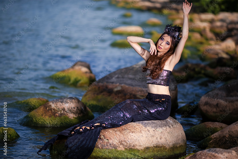 Foto de Mermaid Posing Near Ocean Shore on Rocks While Wearing Seashell Decorated Crown and