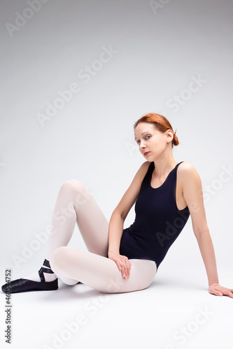 Proudly Looking Gorgeous Professional Female Ballet Dancer in Body Suit Sitting on White Floor.