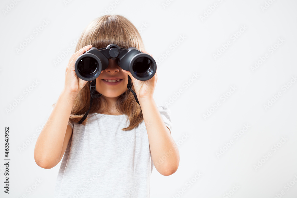 Studio shot portrait of happy little girl who is using binoculars. Copy space on gray background.