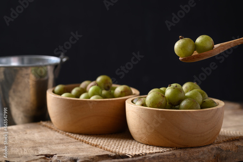 Wild Indian gooseberry or amla in a bowl with spoon on black background, Fruit tree in Asia use in various cuisine, herbal medicine and rich vitamin C