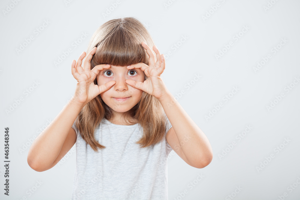 Studio shot portrait of happy little girl who is gesturing. Keep your eyes open gesture. Copy space on gray background. Studio shot portrait of happy little girl who is gesturing. Keep your eyes open gesture. Copy space on gray background.