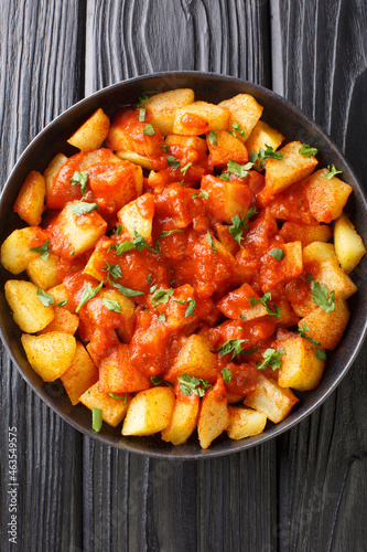 Patatas Bravas is a classic Spanish dish of fried potato cubes served with a spicy dipping sauce close up in the plate on the table. Vertical top view from above