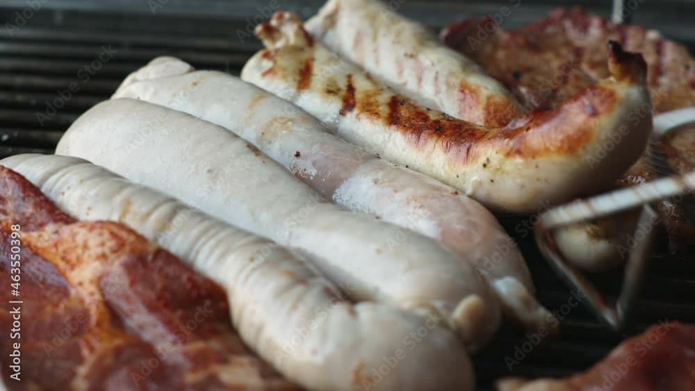 On a grill, fresh German bratwursts are turned for the first time and have a slightly brown side. On a grill, fresh German bratwursts are turned for the first time and have a slightly brown side.
