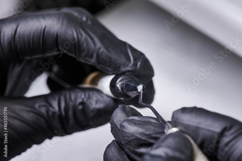 Close up of doctor hands in black sterile gloves preparing bracket bonding paste. Specialist holding dental instrument and adhesive paste for braces placement. Concept of orthodontic treatment