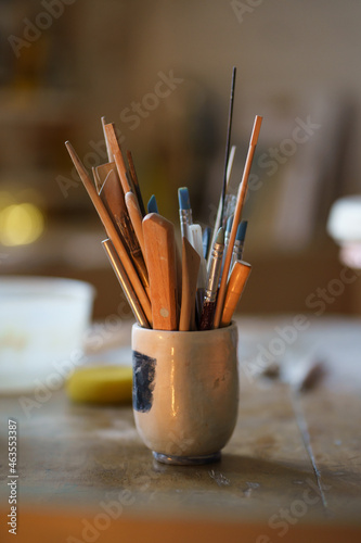 Paint brushes with pottery shaping tools in bowl on wooden table. Ceramics making equipment in creative art space, potter studio or handicraft clay molding workshop interior. Craftsmanship concept