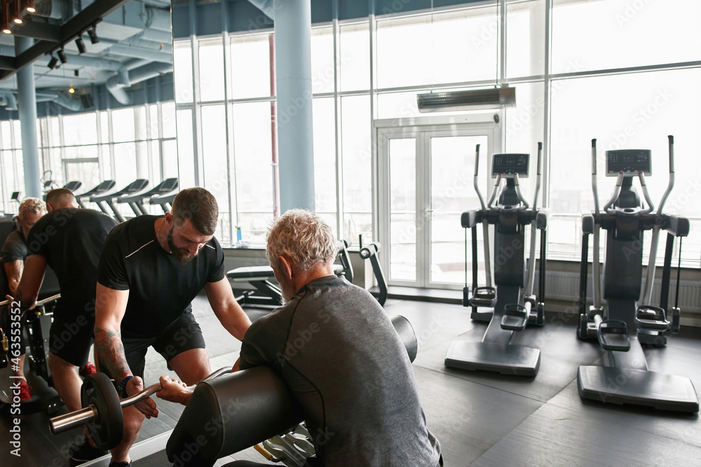 Fototapeta premium Athletic grandfather training powerlifting with trainers support