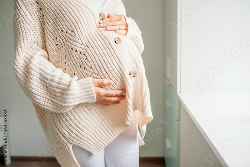 Young beautiful woman in the third trimester of pregnancy. Cropped shot of pregnant woman in knitted sweater with hands on belly photo