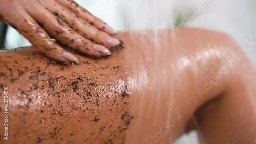 A woman in good athletic shape, sexy, in beige underwear, stands bath among plants, greenery. Washes away coffee scrub from thighs priests water from shower, moves hand. Cleansing, soft skin self-care